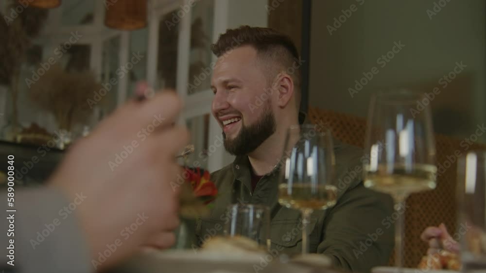 Caucasian man sits in modern gastro cafe, eats delicious dish and talks to friends. Group of people celebrate birthday, have family dinner, spend weekend together in restaurant. Public eating concept. Caucasian man sits in modern gastro cafe, eats delicious dish and talks to friends. Group of people celebrate birthday, have family dinner, spend weekend together in restaurant. Public eating concept.