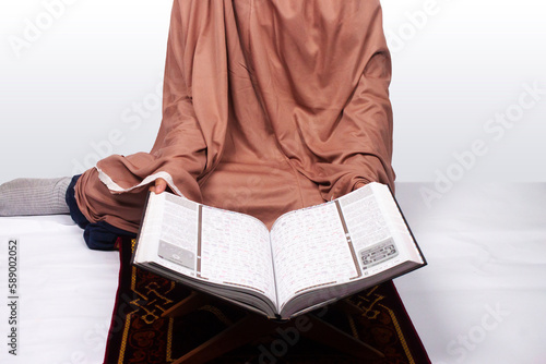 Islamic moslem woman praying Koran or Quran on praying carpet sajadah wearing traditional dress