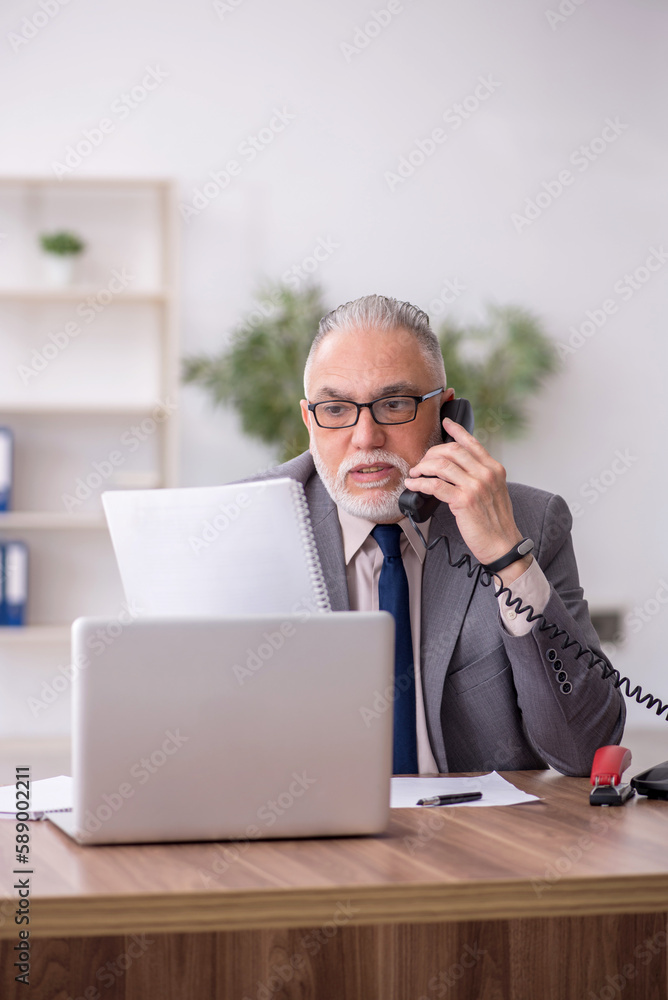 Old male employee speaking by phone at workplace Old male employee speaking by phone at workplace