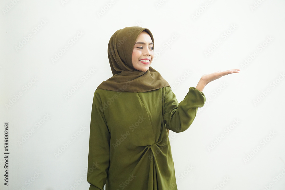 Smiling beautiful asian woman in green dress and hijab pointing to copy space with palms, showing advertising products and confidently looking at camera isolated over white background. Smiling beautiful asian woman in green dress and hijab pointing to copy space with palms, showing advertising products and confidently looking at camera isolated over white background.