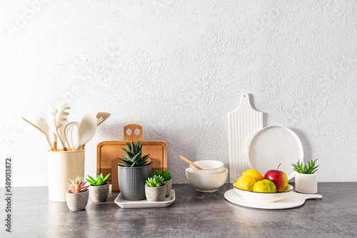 a set of various dishes, tools, a bowl of fruit on a stone countertop opposite a gray textured wall. space for text. still life.