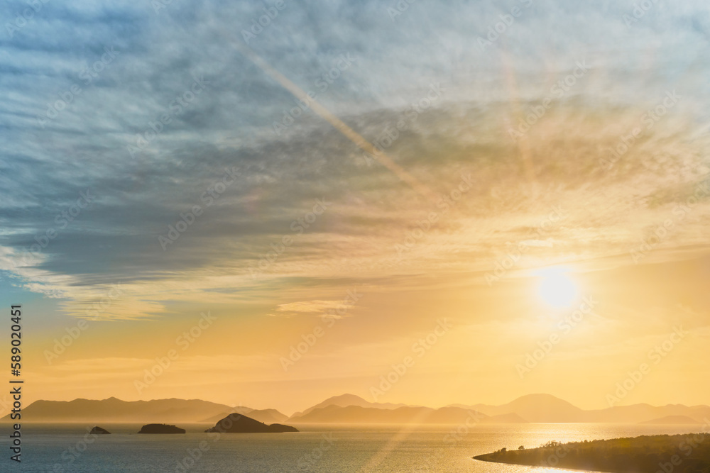 Naklejka premium Scenic sunset on the Aegean coast of Turkey, island in the golden sunlight of the sunset, the idea of landscape and vacation at sea, a break from the bustle of the city