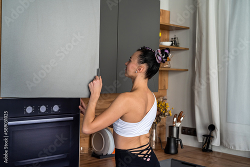 Confident young woman in sportswear drinking a protein shake while standing in the kitchen.