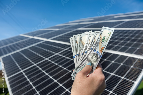 Human hands with a large amount of dollars in front of solar panels.