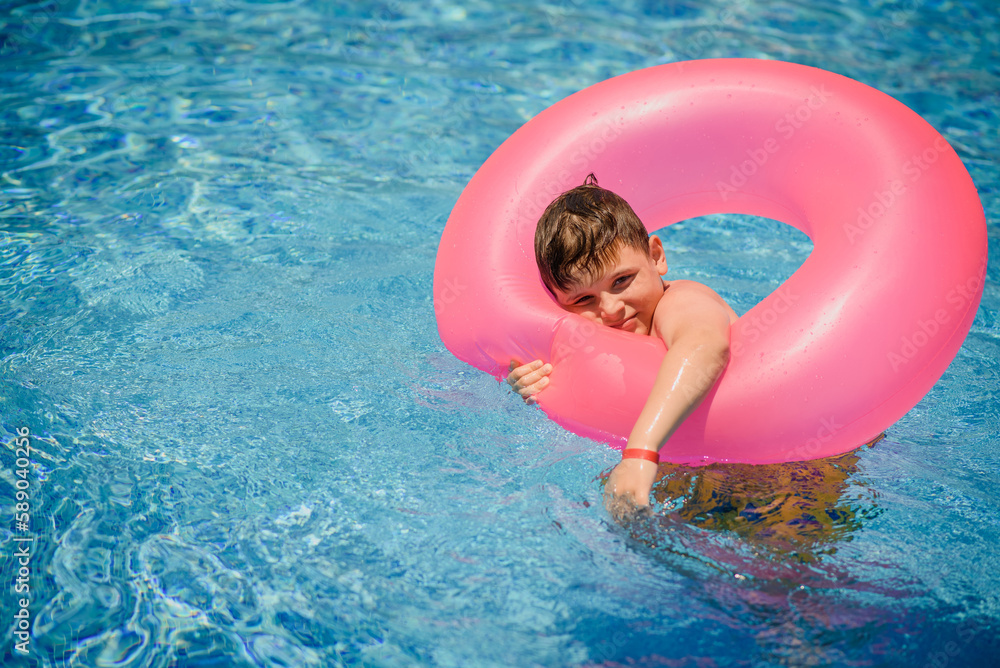 Little boy kid, is swimming with an inflatable circle in the swimming pool.