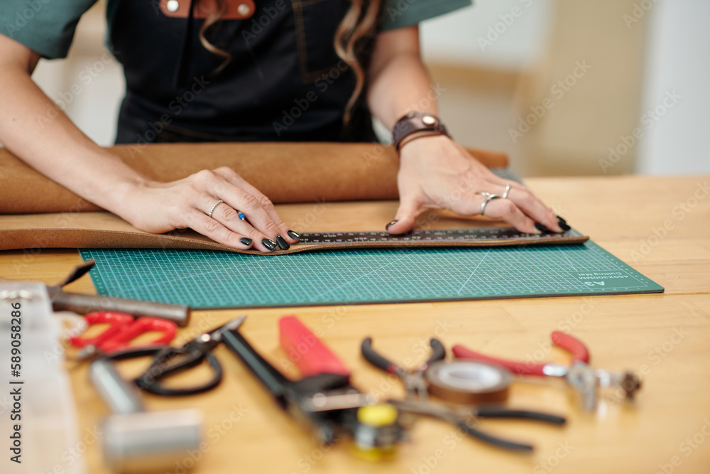 Hands of creative young woman measuring leather piece and taking