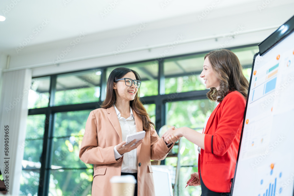 Two young business women meet to analyze the financial chart at the office to discuss the financial situation at the company. A partner sits at a desk with modern documents and equipment. Two young business women meet to analyze the financial chart at the office to discuss the financial situation at the company. A partner sits at a desk with modern documents and equipment.