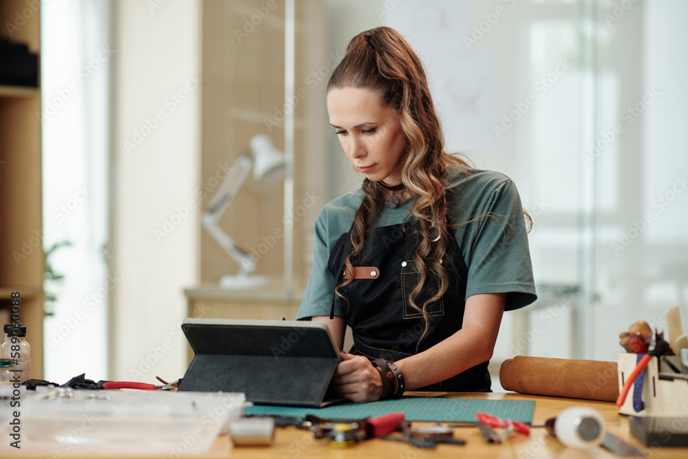 Leather worker checking e-mails and orders from clients on tablet computer