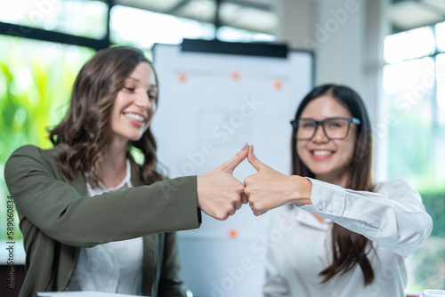 Shot of two young, beautiful, Asian architects, encourage and looking at each other, giving supportive thumb up gesture on teamwork success concept