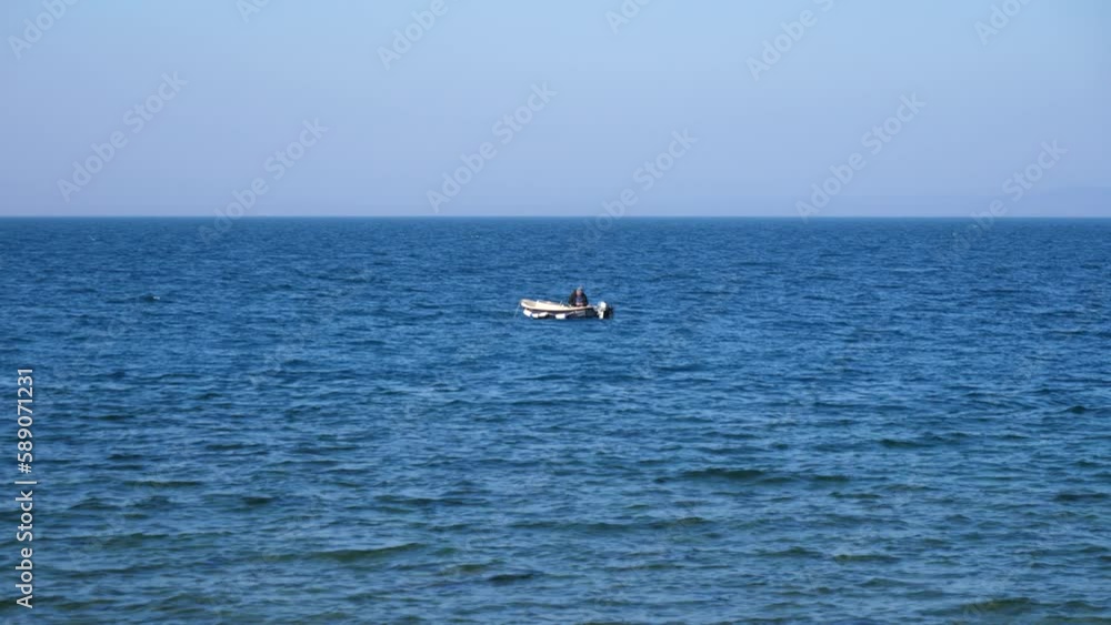 Lone fisherman waits patiently catching fish in open ocean water on sunny day