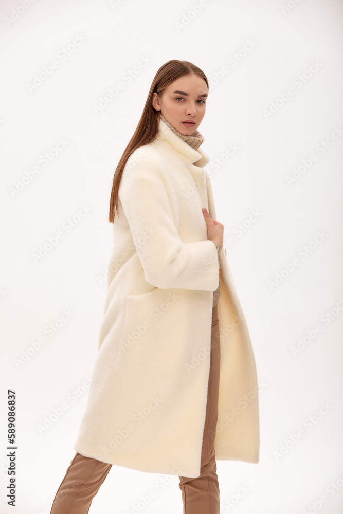 Fashionable self-confident girl in a light faux fur coat. Modern fashion trend for fur coats made of faux fur. Model posing in a fur coat on a light background Fashionable self-confident girl in a light faux fur coat. Modern fashion trend for fur coats made of faux fur. Model posing in a fur coat on a light background