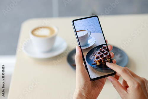 Female hands holding smartphone, taking photograph of her breakfast at a cafe. Concept of sharing food photo on social media.