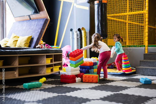 Принти на полотні Two sisters playing at kids play center while build with colored plastic blocks