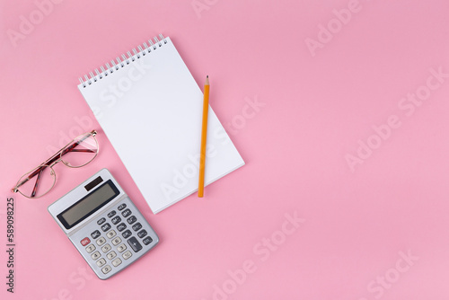 Open notebook pencil and calculator on pink background Business life concept Top view