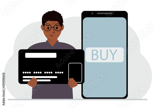A man holds a huge credit card next to a smartphone with a Buy button on the screen. The concept of online payments with payment via mobile phone.