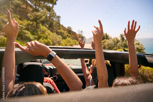 Group Of Laughing Female Friends Putting Hands Through Sunroof Open Top Car On Road Trip photo