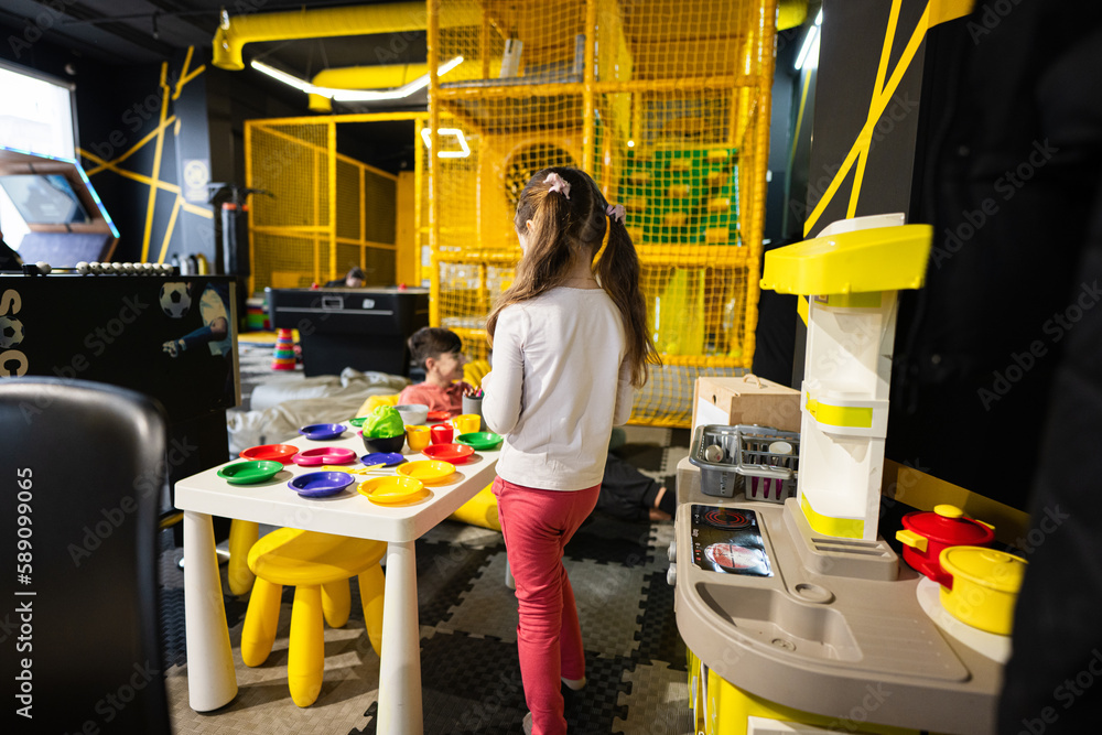 Preschooler girl playing in kids kitchen at children play center.