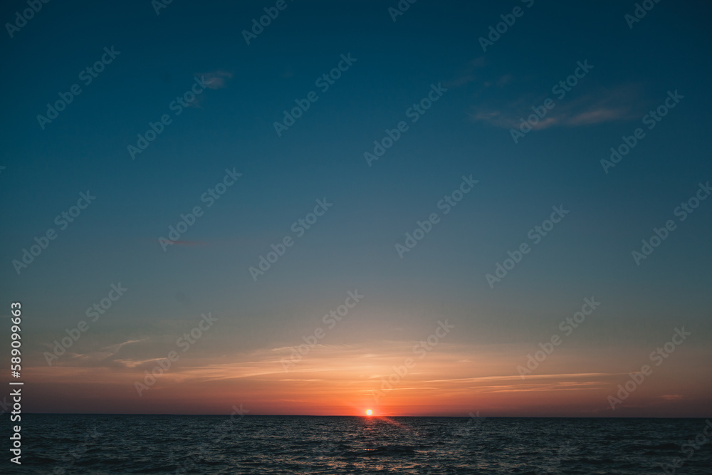 Fototapeta premium Sun set with orange and blue gradient sky windy weather clouds lake sea waves
