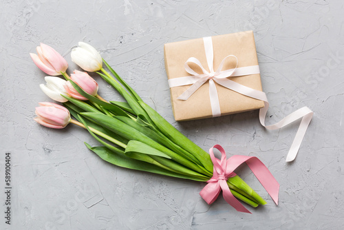 Pink tulips flowers and gift or present box on colored table background. Mothers Day, Birthday, Womens Day, celebration concept. Space for text top view