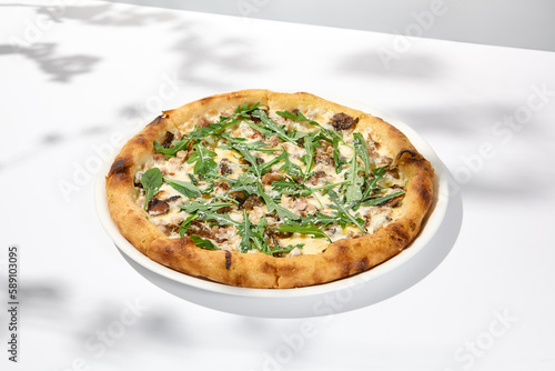 Mushroom pizza with cheese and arugula on white background with shadows. Italian pizza with porcini mushrooms on white table and hard shadows Cheese pizza in trendy style Modern italian food