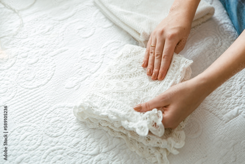 Woman folding laundry and towels in bedroom, organizing clothes in boxes and baskets. Concept of konmari folding system. Tidy up wardrobe Woman folding laundry and towels in bedroom, organizing clothes in boxes and baskets. Concept of konmari folding system. Tidy up wardrobe