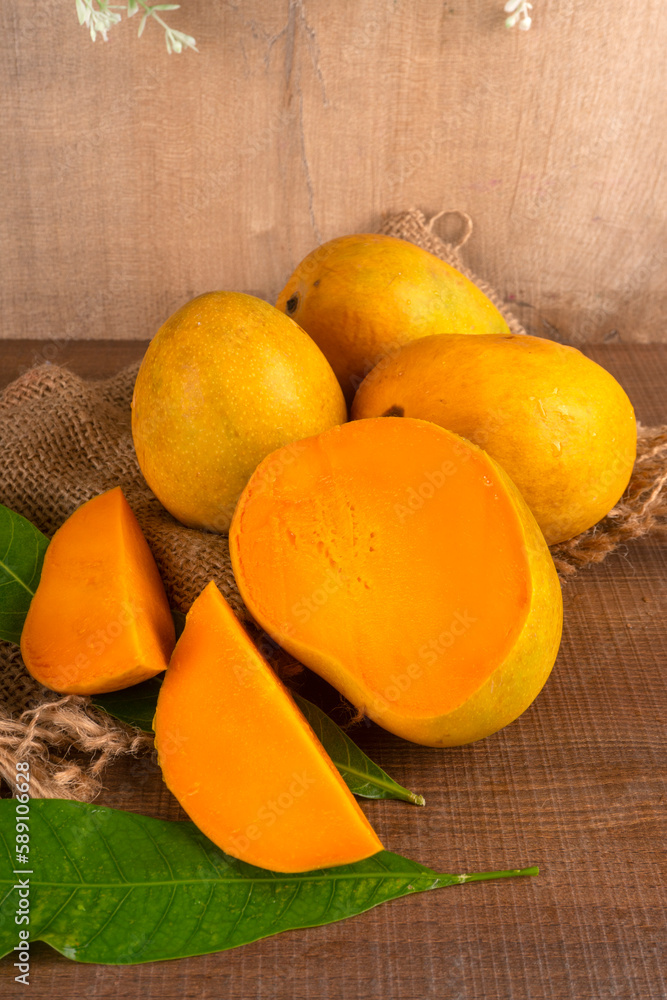 Ripe yellow Mango with cut in half and green leaf isolated on wooden background.