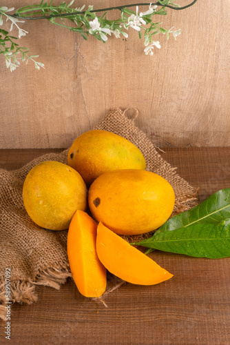 Ripe yellow Mango with cut in half and green leaf isolated on wooden background.