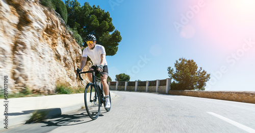 Man Adult on a racing bike climbing the hill at mediterranean sea landscape coastal road on mallorca balearic island photo