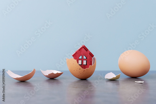 Tiny house in eggs shell over blue background with copy space. Conceptual Easter greeting card