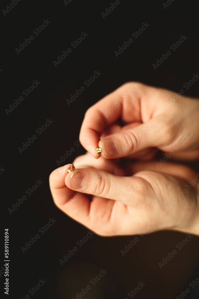 Vertical closeup of two hands holding gold studs against a black background Vertical closeup of two hands holding gold studs against a black background