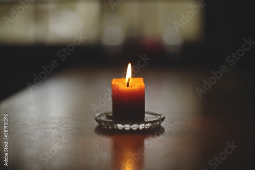 Closeup shot of a lit candle on a glass saucer with a reflection on a wooden table