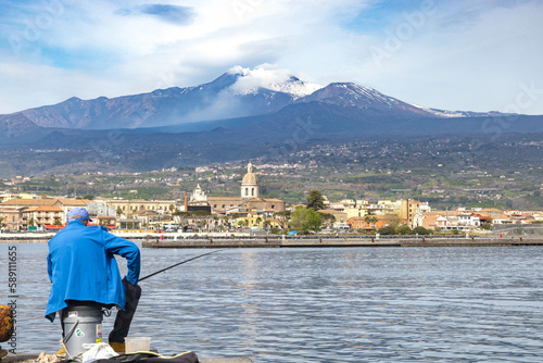 Riposto vista dal porto marinaro con pescatore in primo piano e con il vulcano Etna sullo sfondo - Sicilia photo