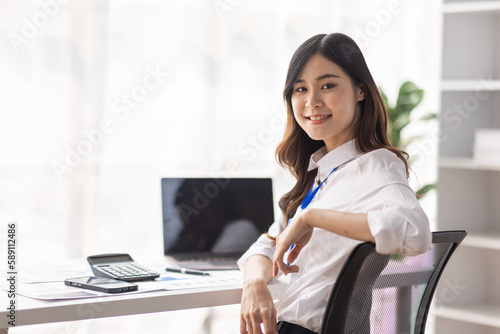 Charming Young asian businesswoman sitting on laptop computer in the office, asian employee business making report calculating balance Internal Revenue Service checking document.