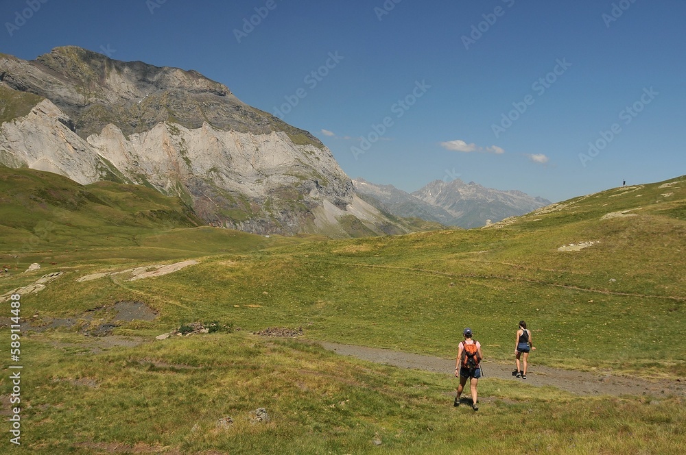 Group of tourists exploring the Catalan Pyrenees with tall rocky mountains looming over green fields