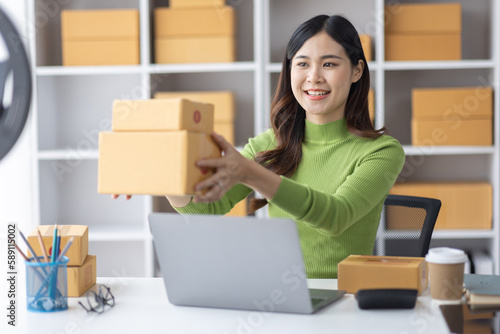 Startup SME small business entrepreneur freelance Asian woman using a laptop with box merchant seller checking customer address order confirming parcel SME delivery idea concept.