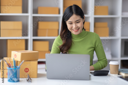 Startup SME small business entrepreneur freelance Asian woman using a laptop with box merchant seller checking customer address order confirming parcel SME delivery idea concept. © David