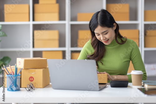 Startup SME small business entrepreneur freelance Asian woman using a laptop with box merchant seller checking customer address order confirming parcel SME delivery idea concept. © David