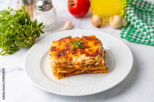 Portion of ground beef lasagna topped with melted cheese and garnished with fresh parsley served on a plate in close view for a menu