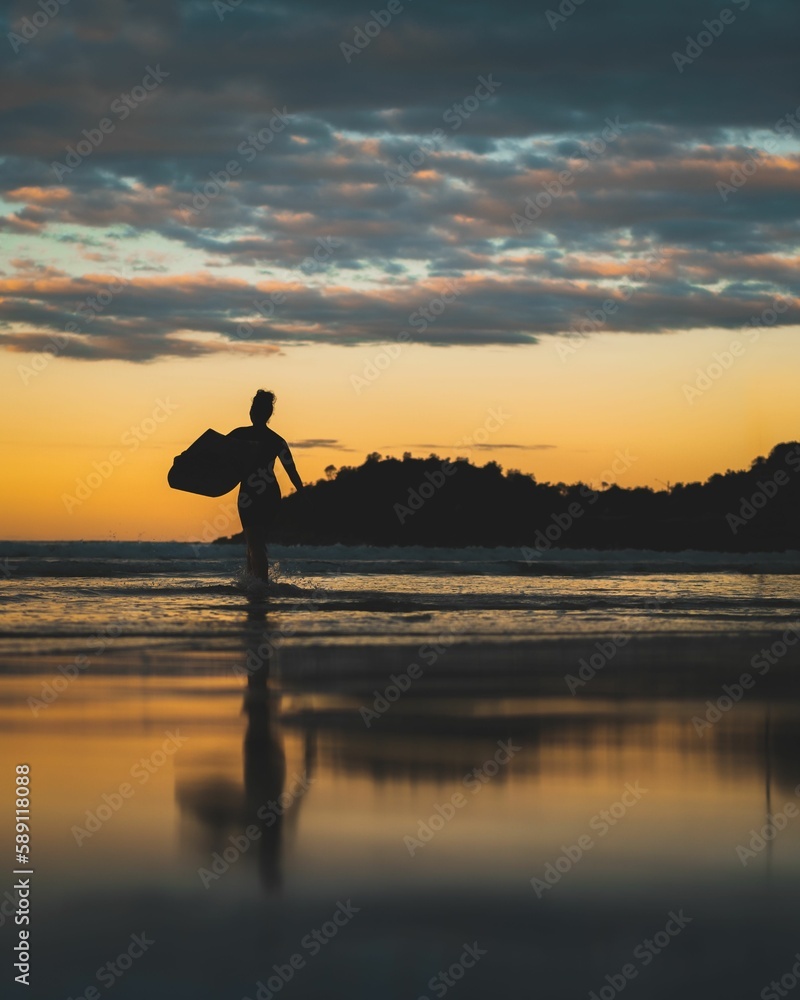 Vertical shot of a girl surfer's silhouette on a beach in Manly, Sydney, NSW, Australia at sunset