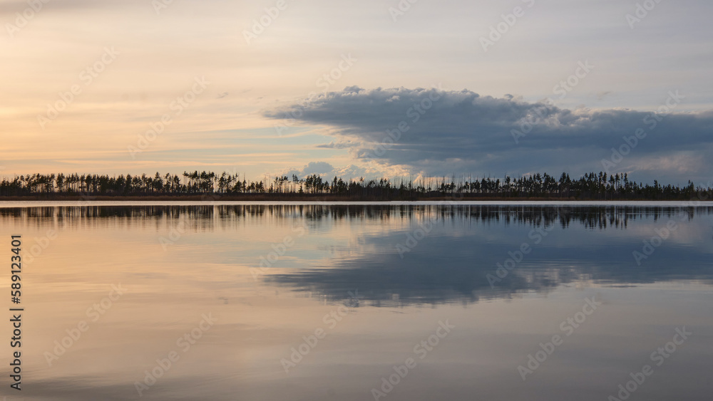 Silhouette of forest on horizon behind lake during sunset: reflection, bizarre clouds, bright evening sky, nature of Northern Europe.
