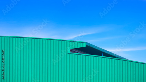Green Corrugated metal curved Roof of large Warehouse Building in modern style against blue sky Background