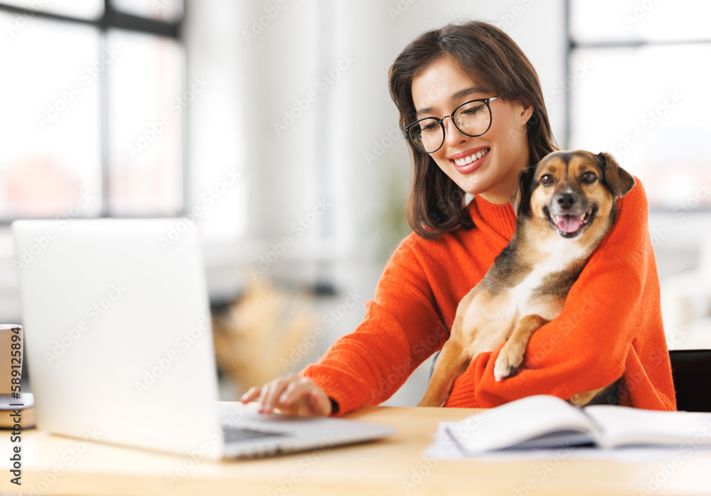 happy woman freelancer working on laptop remotely from home together with pet dog