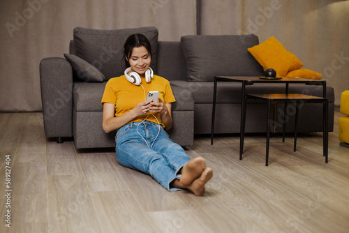Happy indian or arabian girl resting on cozy sofa at home, listening to music