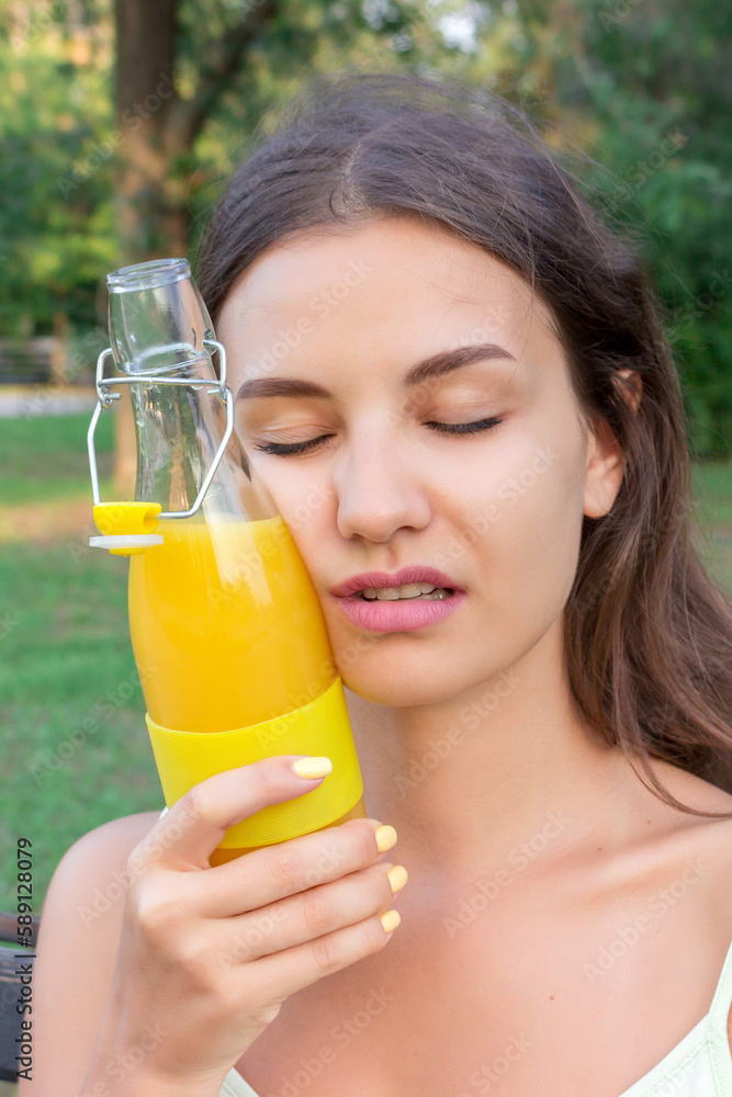 Young woman is tired of hot weather. Girl is holding a cold bottle of juice near forehead Young woman is tired of hot weather. Girl is holding a cold bottle of juice near forehead