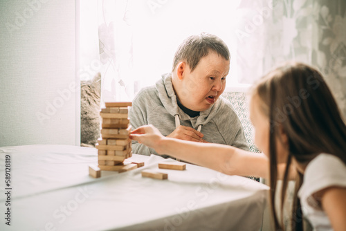 elderly woman with down syndrome and an Asian girl play in tower from wooden blocks