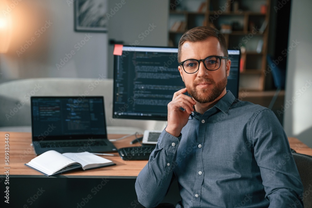 Software developer is sitting and posing. Man in formal clothes is working in the modern office. Using computer Software developer is sitting and posing. Man in formal clothes is working in the modern office. Using computer