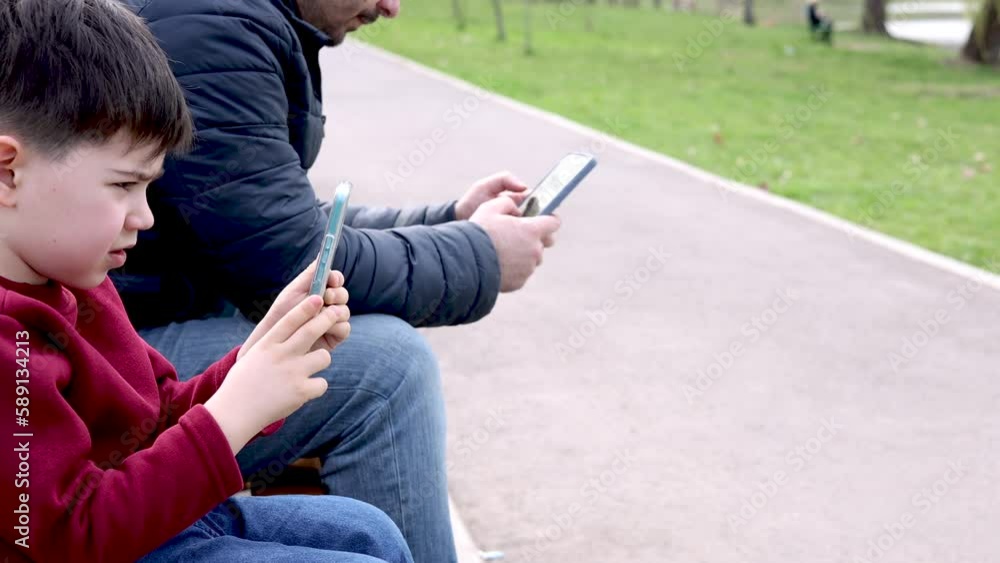 daddy man and little boy kid child sitting on park bench playing with mobile phone,smartphone.different generations addicted by device technology,park environment.4k slow motion dad and son daddy man and little boy kid child sitting on park bench playing with mobile phone,smartphone.different generations addicted by device technology,park environment.4k slow motion dad and son