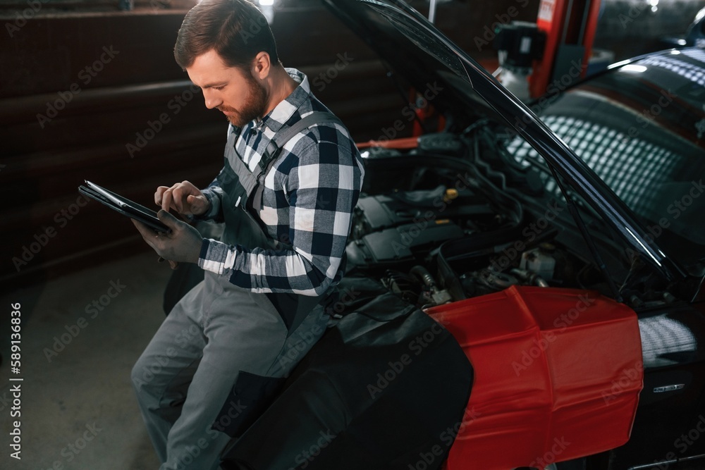 With tablet in hands. Man in uniform is working in the auto salon With tablet in hands. Man in uniform is working in the auto salon