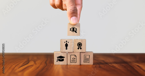 HRM and recruitment concept. Job search, headhunting and recruitment process. Holding wooden cube with icons of education, qualification, cv, resume, skills and experience on smart grey background