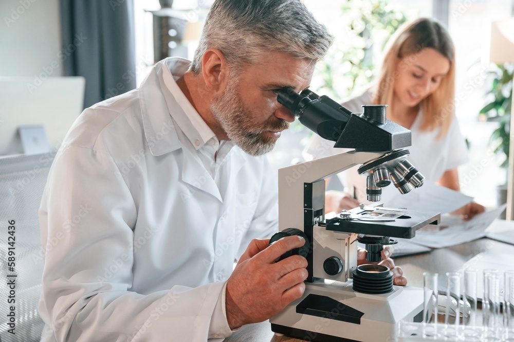 Focused on work. Two doctors are indoors together. Senior man with young woman Focused on work. Two doctors are indoors together. Senior man with young woman